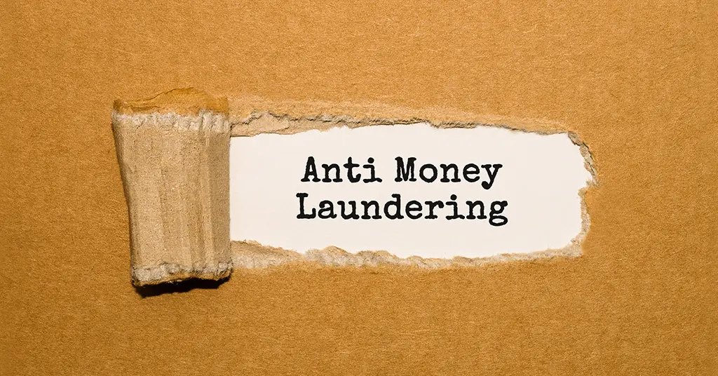 Written text of anti-money laundering appearing behind torn brown paper.